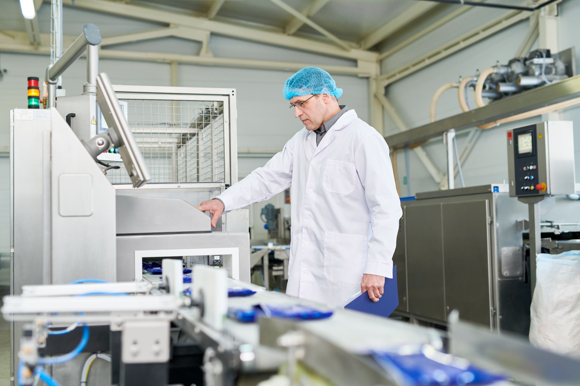 Serious experienced male food technologist in sterile clothes changing program of production line while working in packaging shop